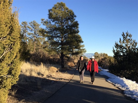 Canyon Rim Trail at golden hour during the late winter with two walkers coming towards the viewer smiling and wearing jackets and hats