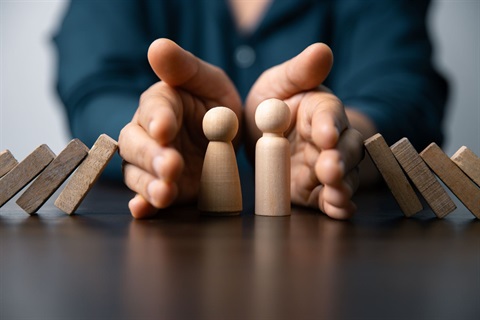 Emergency types image showing hands protecting two people represented by wooden pieces as dominos fall around them.