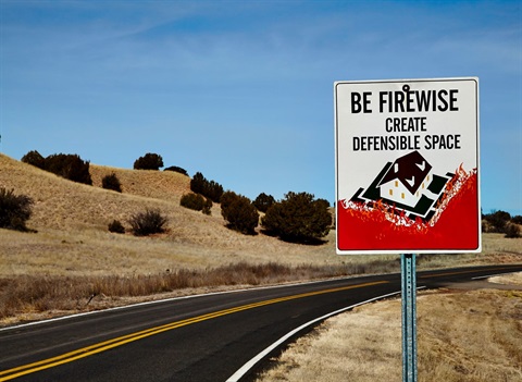 Photograph of a rural desert highway. In the foreground, a street sign reads 