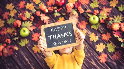 Happy Thanksgiving Image with a child laying on a bed of leaves and apples holding a chalk board that says happy thanksgiving