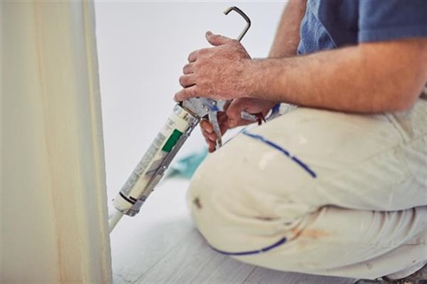 Photo of a man sealing at base of wall with caulk