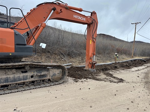 A large, orange excavator performs construction work on a dirt road