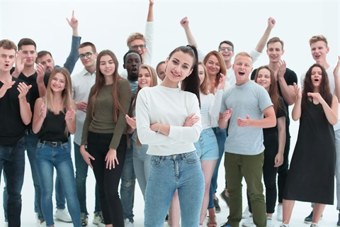 A group of teenagers cheering behind one teenage girl who is looking confidently at the camera