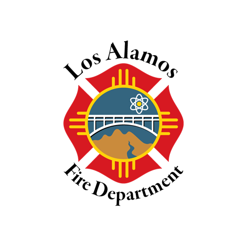 This image depicts the LAFD bridge logo. This is a circular logo within a yellow Zia depicting a white bridge across brown hills and a blue river with a yellow sun surrounded by the white atomic structure in a blue sky.